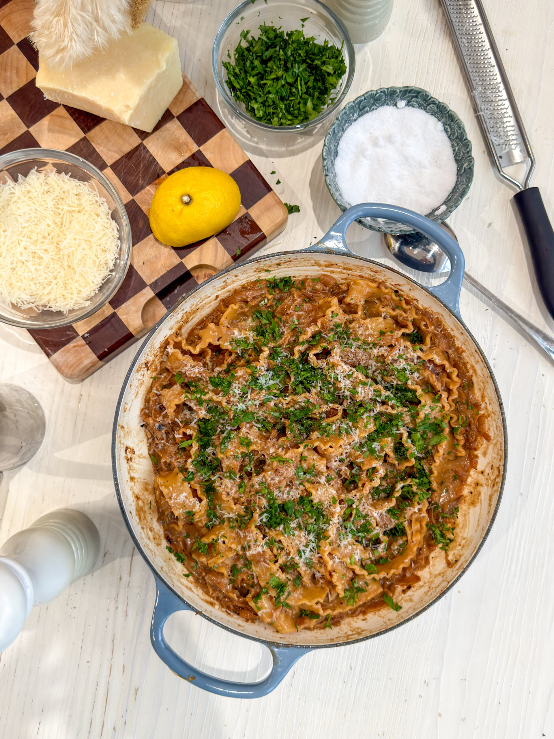 Caramelized onion pasta with ruffled mafaldine noodles in a blue Le Creuset braiser, topped with fresh parsley and grated Parmesan cheese.